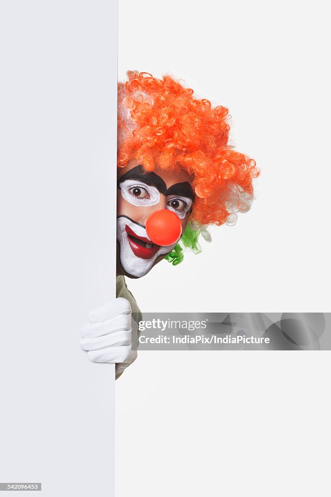 Happy clown hiding behind billboard over white background