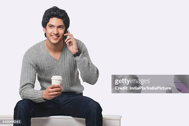 young man talking on cell phone while holding disposable cup - v hals stockfoto's en -beelden