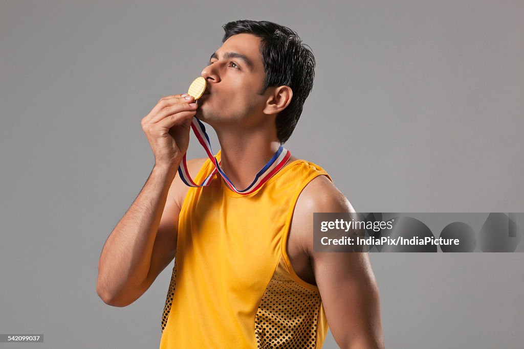 Young man in spots wear kissing gold medal isolated over gray background
