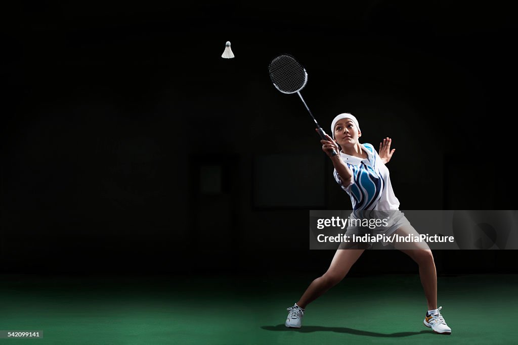 Full length of young woman hitting shuttlecock with badminton racket at court