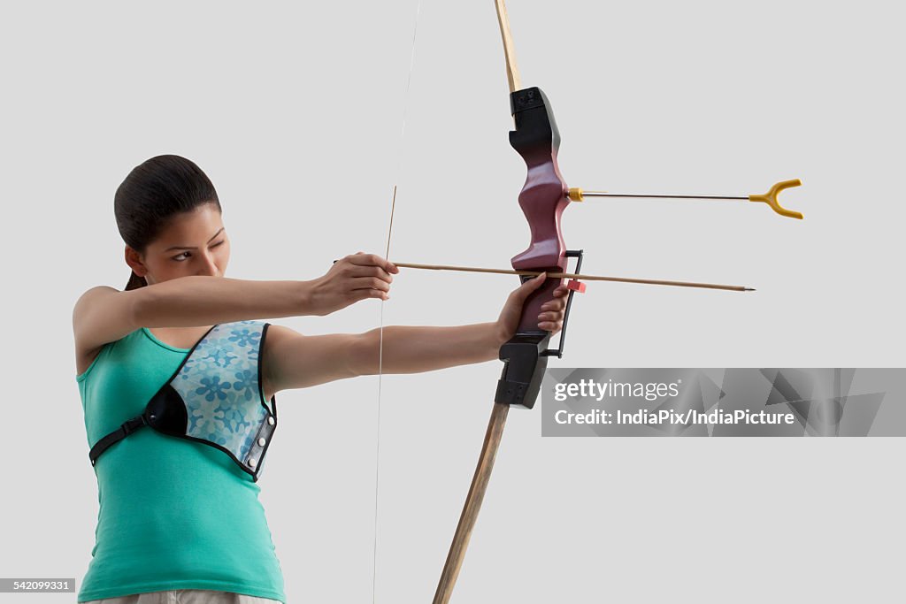 Young female archer practicing archery against gray background