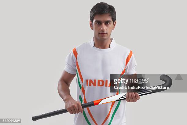 portrait of confident young man holding hockey stick against gray background - hockey background stockfoto's en -beelden