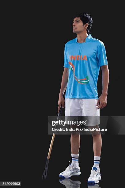 full length of sportsman with hockey stick looking away over black background - hockey background stockfoto's en -beelden