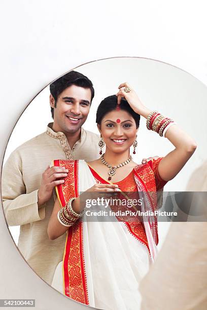 bengali woman putting sindoor on her forehead while husband watches on - bengali sari stockfoto's en -beelden