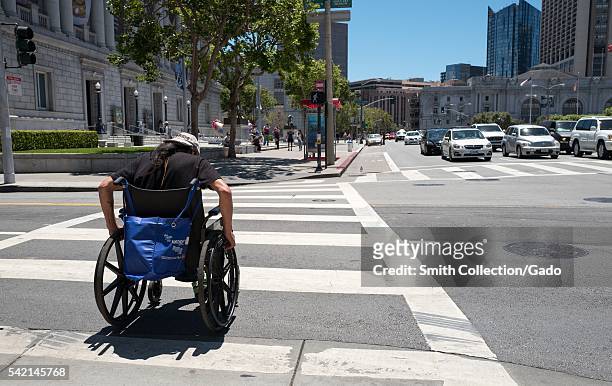 In the Civic Center neighborhood of San Francisco, a disabled homeless man in a wheelchair crosses an intersection, San Francisco, California, 2016. .