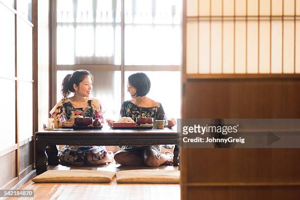 zwei japanische freundinnen sitzen auf boden essen nudeln - auf dem boden sitzen stock-fotos und bilder