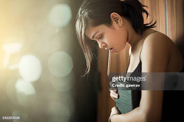 girl looking down and thinking while holding book and pencil. - girl looking down stock pictures, royalty-free photos & images