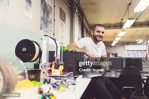 Young man using a 3D printer in a construction workshop Young man using a 3D printer in a construction workshop