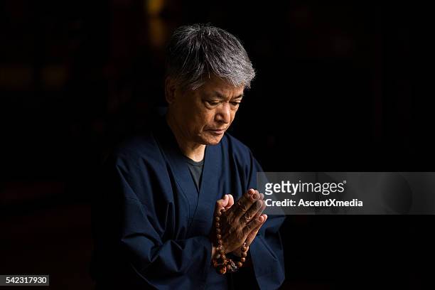 senior japanese man praying at a temple - godsdienstige gebouwen stockfoto's en -beelden