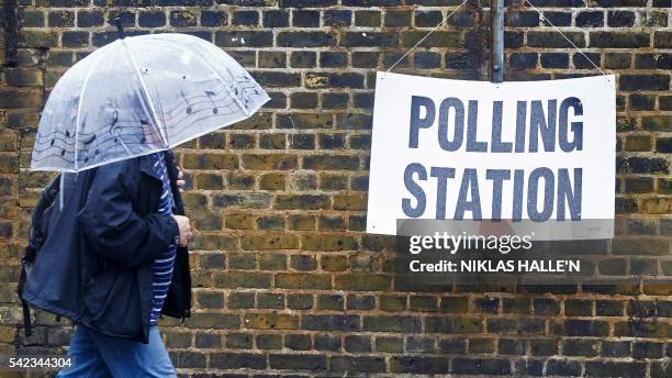 Man shelters from the rain as he arrives at a polling station in London on June 23 as Britain holds a referendum on wether to stay in, or leave the...