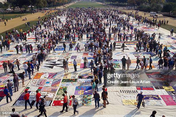 Demonstrators gather in hommage of the victims of AIDS, walking along a large patchwork quilt representing the dead.