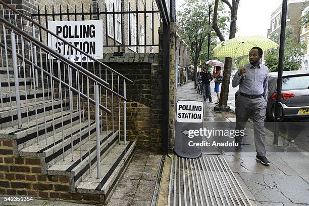 Man holding an umbrella passes by a polling station during the British EU Referendum in London, United Kingdom on June 23, 2016. Voting has begun in...