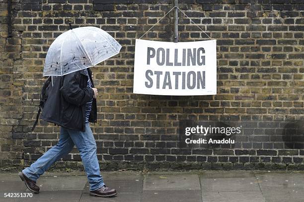 Man holding an umbrella passes by a polling station sign during the British EU Referendum in London, United Kingdom on June 23, 2016. Voting has...