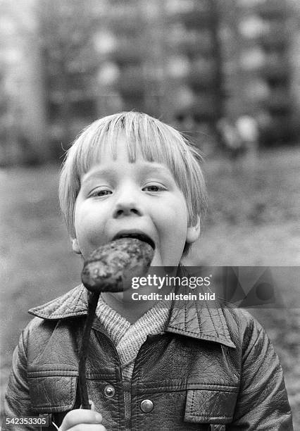 Junge lässt sich eine geröstete Kartoffel am Stecken schmecken.1977