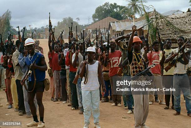 Young recruits for the National Patriotic Front of Liberia raise their weapons at a training camp in Gborplay, Liberia. Responding to years of...