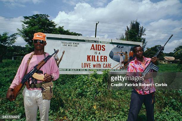 Pausing during their violent campaign to take the Liberian capital, two members of the National Patriotic Front of Liberia stand near a billboard...