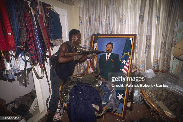 Member of the National Patriotic Front of Liberia points a gun at a portrait of President Samuel Doe after raiding the home of Jackson Doe, the...