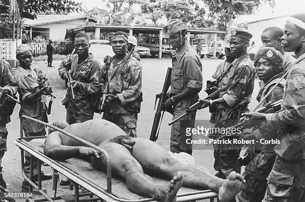 Liberian soldiers pose with their rifles around the displayed dead body of President Samuel Doe during the Liberian Civil War. Prince Yormie Johnson,...