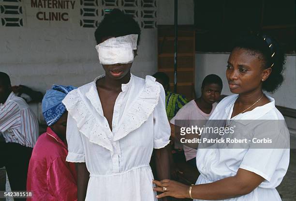 Nurse helps a young woman blinded during the Liberian Civil War. The civil war and interfactional fighting created an exodus of refugees who headed...