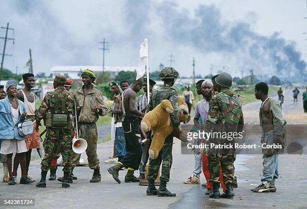 Rebels and ECOMOG soldiers chat on a road in Monrovia during the Liberian Civil War. One NPFL rebel brandishes a white flag while an ECOMOG soldier...