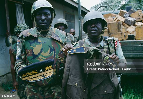 Nigerian soldiers from ECOMOG hold up a military uniform as they patrol the Caldwell front during the Liberian Civil War. In 1989, Charles Taylor,...