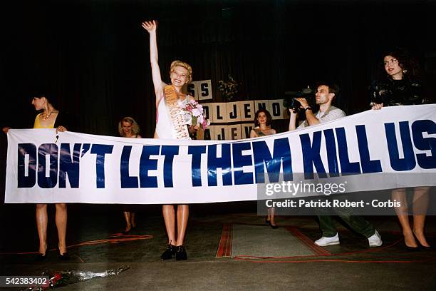 Pageant winner Inela Nogic stands behind a banner as she waves to the audience during the 1993 Miss Sarajevo Pageant. The banner reads "DON'T LET...