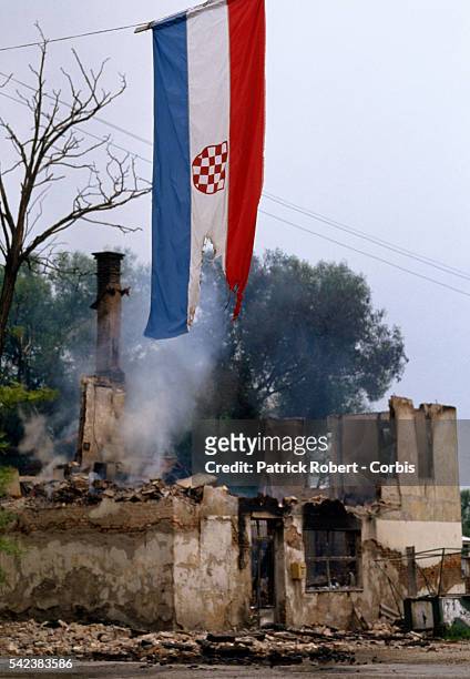 Damaged Croatian flag hangs near a burned Muslim home on the eastern frontline of Travnik during the Yugoslavian Civil War. Conflict among the...
