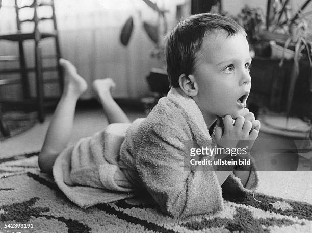 Kind vor dem Fernsehgerät. Es liegt im Bademantel auf dem Boden und hat einen staunenden Gesichtsausdruck.1972
