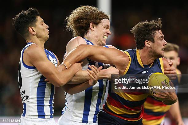 Lindsay Thomas and Ben Brown of the Kangaroos tackle Kyle Hartigan of the Crows during the 2016 AFL Round 14 match between the Adelaide Crows and the...