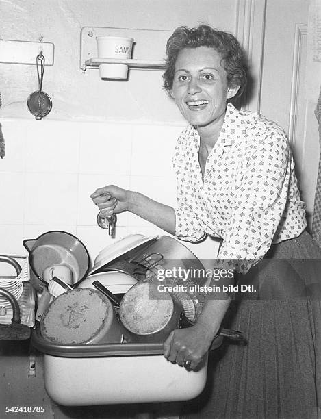 Frau steht am Waschbecken, in dem sichGeschirr und Töpfe stapeln- um 1956