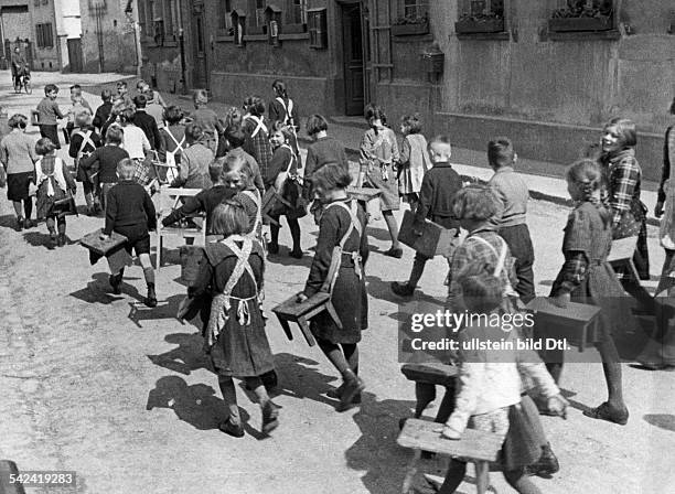 Kinder laufen mit ihren Stühlen undHockern die Strasse entlang zur Schule,um sich bei der dort stattfindendenFilmvorführung einen Sitzplatz zu...