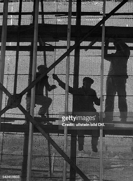 Silhouetten von Bauarbeitern, dieDrahtnetze am Stahlgerüst befestigen.um 1930