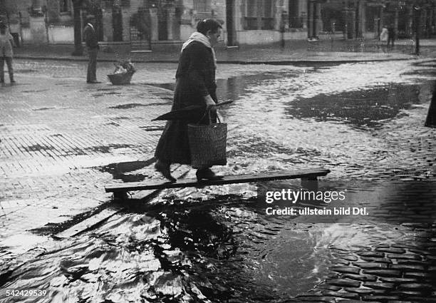 Buenos Aires im Regen" - eine Frau übequert auf einem improviesierten Holzsteg eine überschwemmte Straße in Buenos Aires