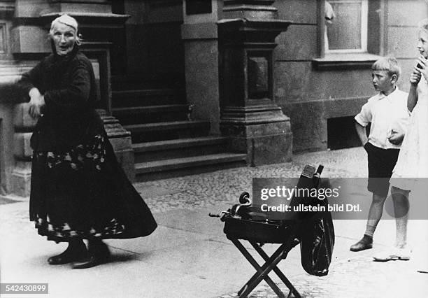 Eine alte Frau verdient sich ihren Lebensunterhalt, indem sie zu Musik aus einem Gramophon auf dem Gehweg tanztum 1950