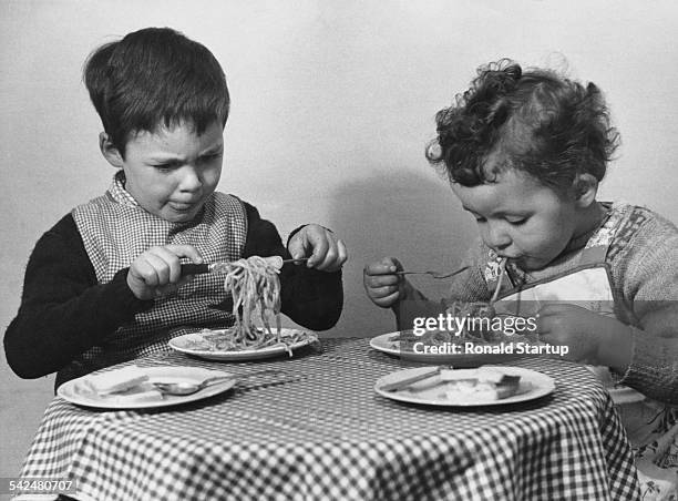 Two children doing their best to eat a meal of spaghetti, May 1952. Original publication: Picture Post - 5865 - There's Simply No End To It! - pub....