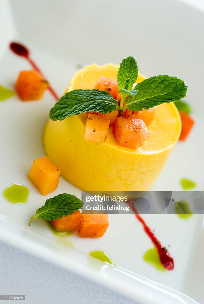 Yellow dessert with fruit and mint on white plate