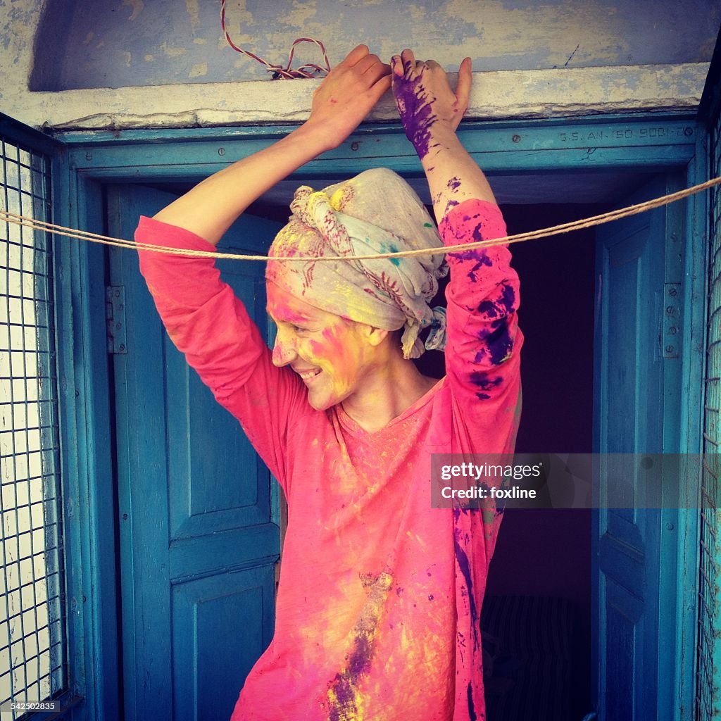 Young woman with headscarf and painted face leaning against blue door