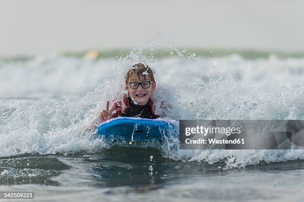 portrait of boy with surfboard showing victory sign - water glasses ストックフォトと画像
