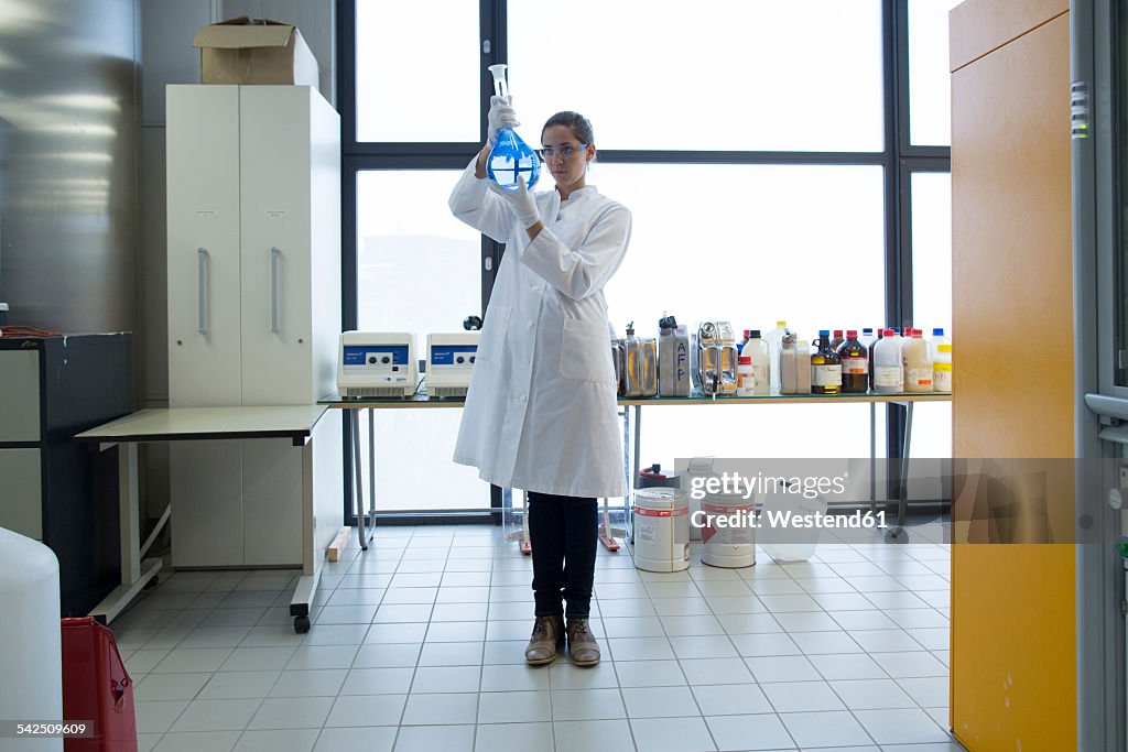 Young female scientist with glass bulb standing in a chemical lab