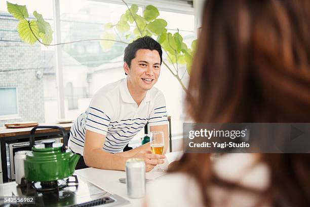 couple drinking beer in the kitchen counter - man sipping beer smiling stockfoto's en -beelden
