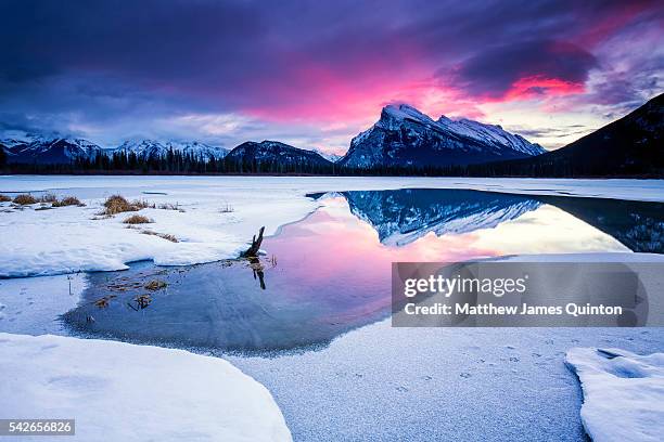 pink sunrise over mountain reflected in partially frozen lake with snow - canada landscape ストックフォトと画像