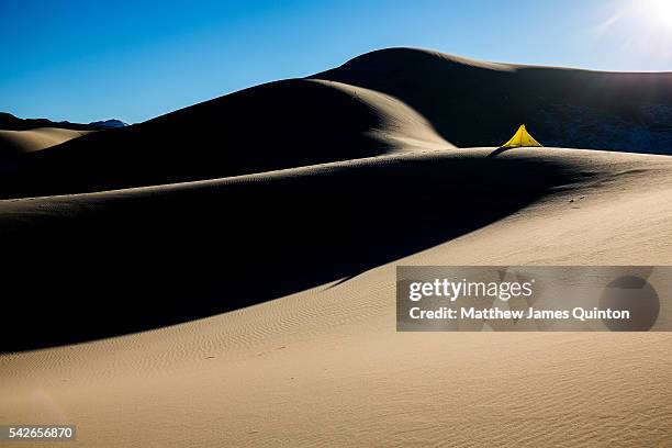 yellow tent on high contrast dunes and sun shining down casting hard light - yellow light effect stock pictures, royalty-free photos & images