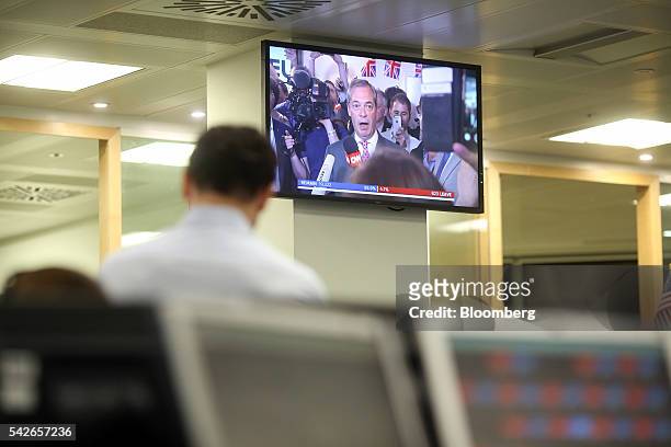 Nigel Farage, leader of the U.K. Independence party , appears on a television displaying a news channel as traders monitor financial data on...