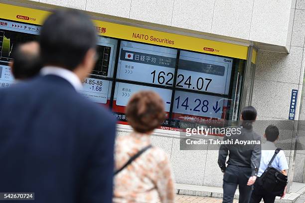 Pedestrians walk in front of an electronic board displaying price of the Nikkei stock average outside of a securities firm on June 24, 2016 in Tokyo,...