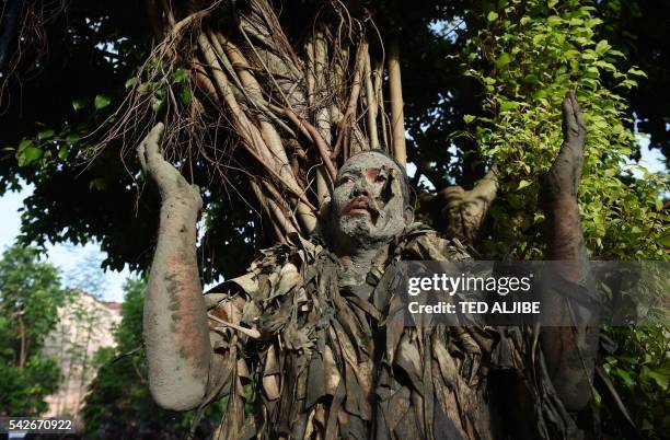 Devotee, covered in mud and wearing costume made from banana leaves, gestures next to a tree as he attends a mass as part of a religious festival in...