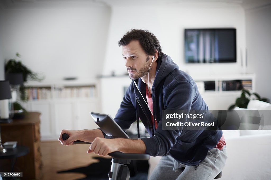 Man with earbuds on exercise bike at home
