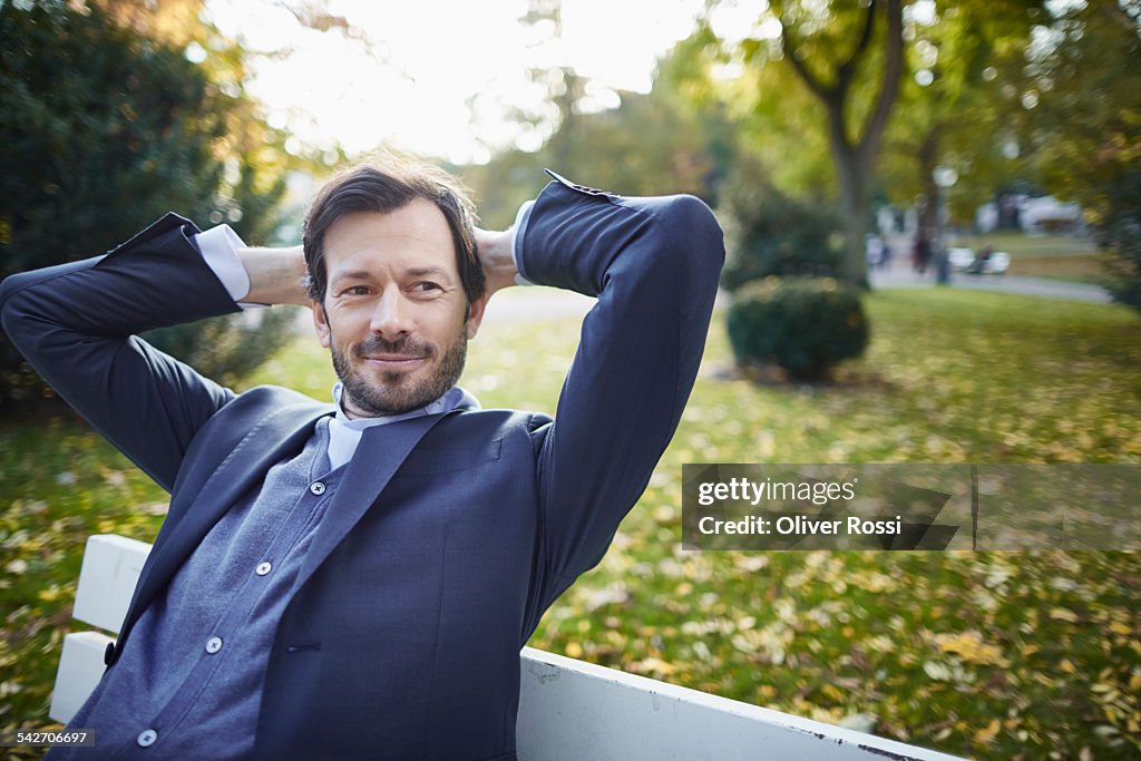 Smiling businessman contemplating on bench in park
