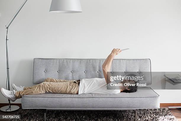 relaxed man lying on couch holding digital tablet - wohnzimmerlampe stock-fotos und bilder