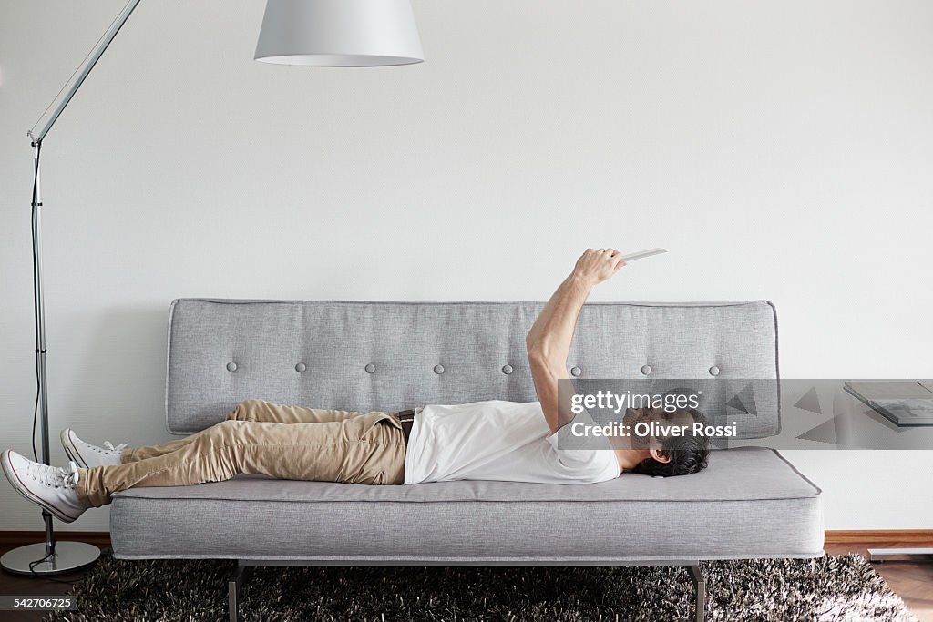 Relaxed man lying on couch holding digital tablet