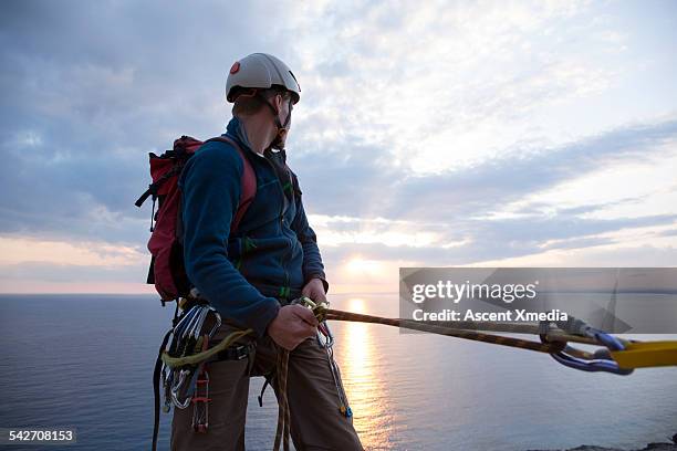 climber pauses in descent, looks back to sea, sun - safety harness stock pictures, royalty-free photos & images